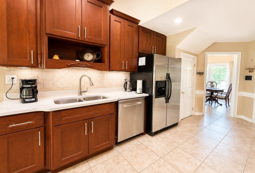 Functional kitchen featuring cherry wood cabinetry, light-toned countertops, a stainless steel double-basin sink with a pull-down faucet, and a tile backsplash
