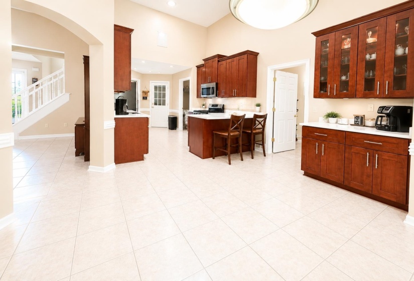 Spacious kitchen featuring high ceilings, light-toned tile flooring, rich wood cabinetry, white countertops, and an integrated kitchen island with seating