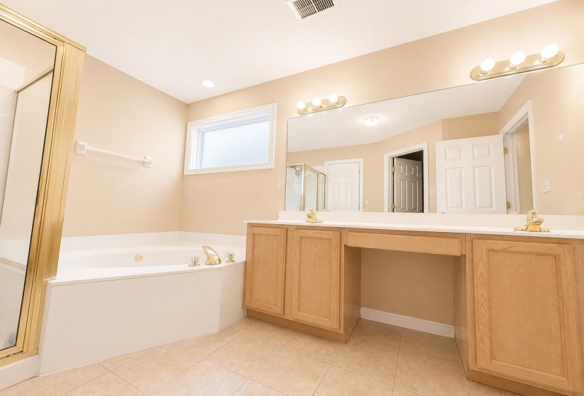 Primary Bathroom featuring a built-in jetted tub, a separate shower enclosure with a brass-finish frame, and tile flooring