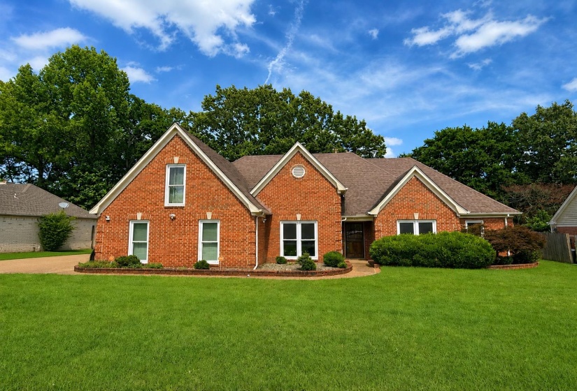 Brick facade residence featuring a front gable, gabled roofline, mature landscaping, and an attached garage with a paved driveway