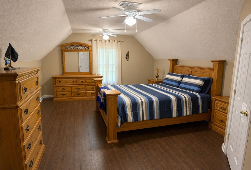 Spacious room featuring wood-finish flooring, an angled ceiling, and two ceiling fans with integrated lighting