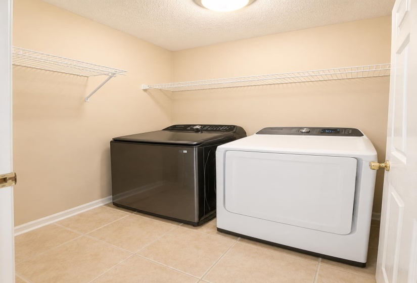 Dedicated laundry space featuring neutral tile flooring, two white wire shelving units, and a flush-mount ceiling light fixture