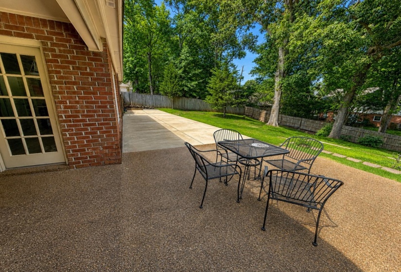 Expansive aggregate patio with an adjacent concrete pathway, framed by a brick exterior and a privacy fence