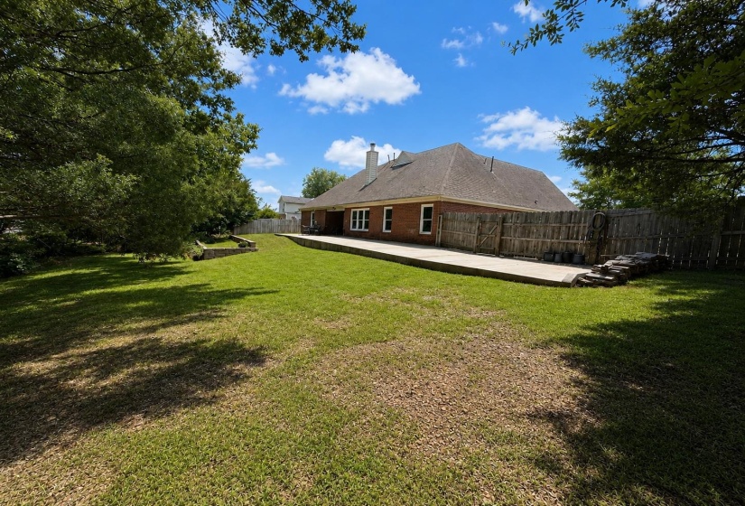 Expansive backyard featuring a large concrete patio, mature trees, and a wooden privacy fence