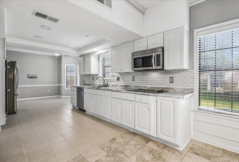 Contemporary kitchen featuring white cabinetry, integrated stainless steel appliances, a subway tile backsplash, and light-toned countertops