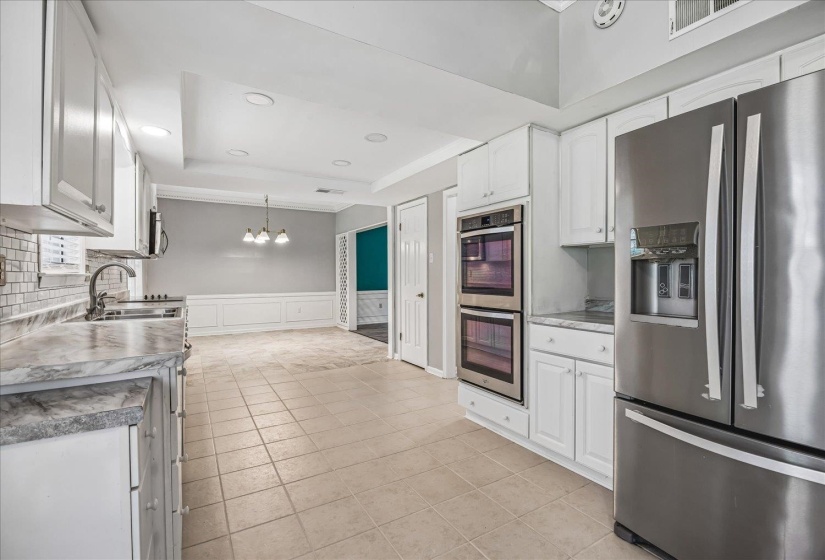Kitchen featuring white cabinetry, light-toned tile flooring, stainless steel double ovens, a stainless steel refrigerator, and a tile backsplash
