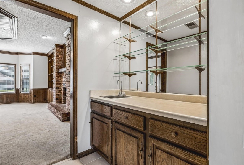 Wet bar featuring wood cabinetry, integrated sink, and glass shelving against a mirrored backdrop