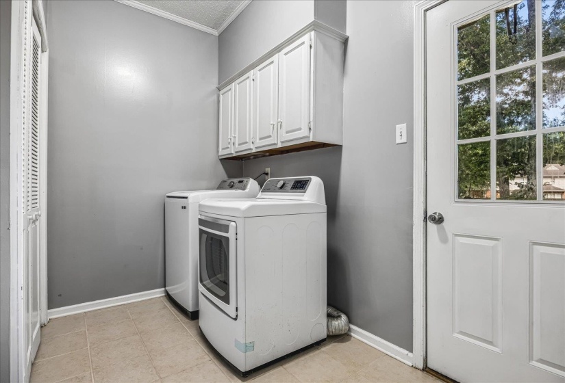 Dedicated laundry space featuring ceramic tile flooring, overhead cabinetry, and an exterior glass-paneled door
