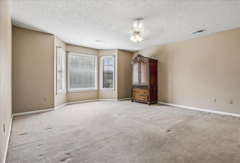 Spacious room featuring multiple bay windows with blinds, neutral-toned walls, and a ceiling fan with integrated lighting