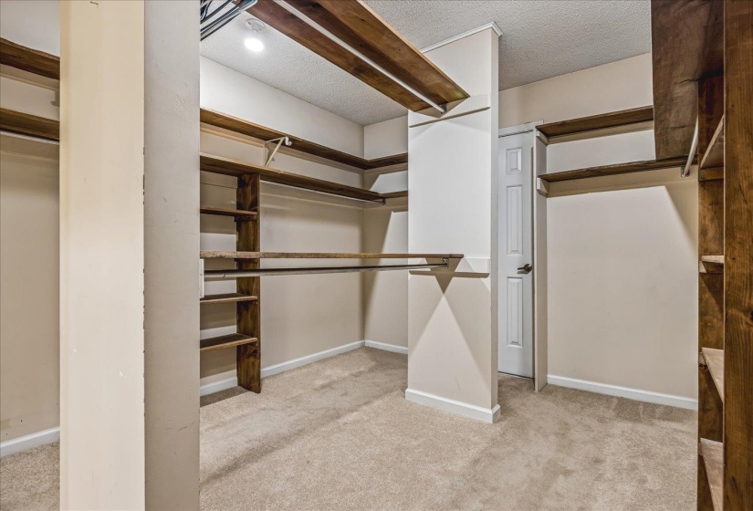 Expansive closet featuring multiple wood-finish shelving units and hanging rods, recessed ceiling lighting, and light neutral carpeting
