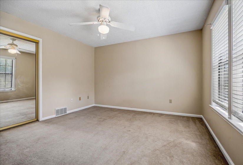 Carpeted room featuring a ceiling fan with integrated lighting, a window with horizontal blinds, a mirrored closet door with a gold-tone frame, and light neutral wall colors