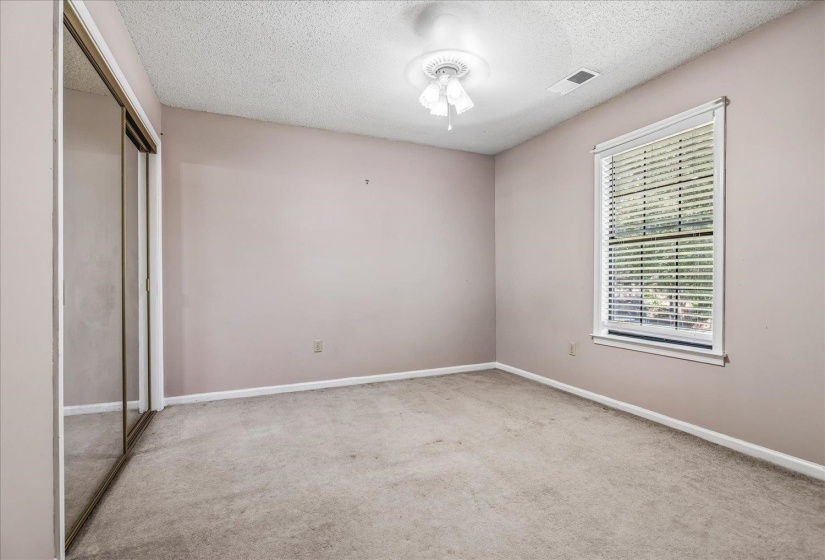 Carpeted interior room featuring a window with blinds, ceiling fan with light fixture, and mirrored sliding closet doors