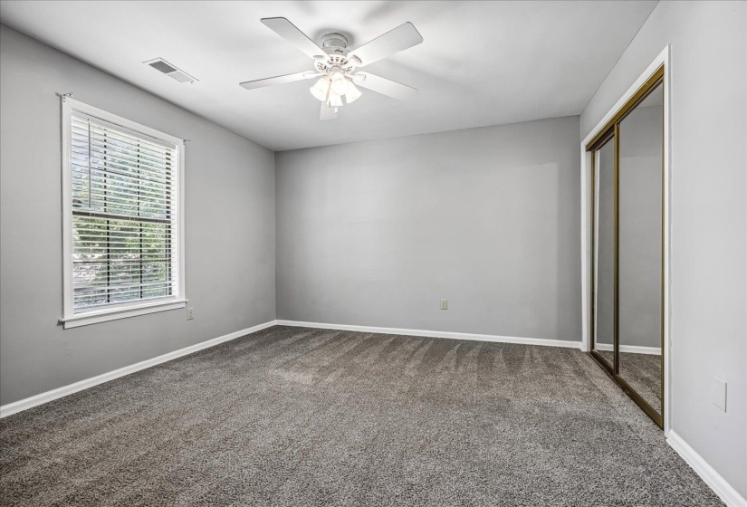 Carpeted room featuring a ceiling fan with integrated lighting, a window with horizontal blinds, and a mirrored sliding closet door