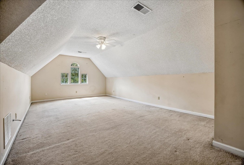 Spacious room featuring vaulted ceilings, a central ceiling fan, and light-colored carpeting