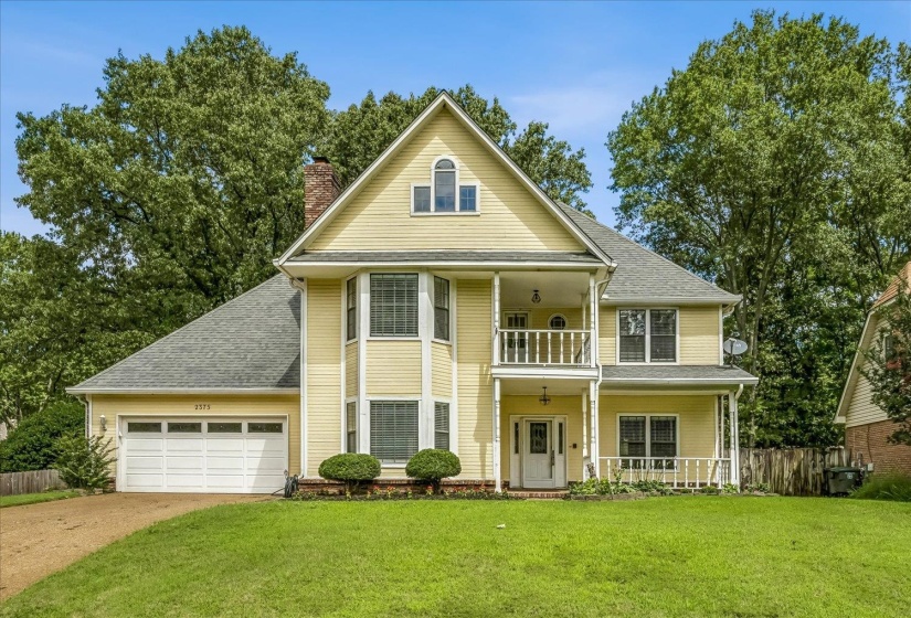 Two-story yellow residence featuring a prominent bay window and a second-level balcony