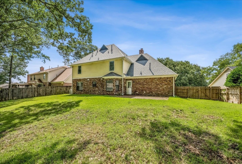 Expansive backyard featuring a lush lawn, brick and siding exterior, a private patio space, and a wooden perimeter fence
