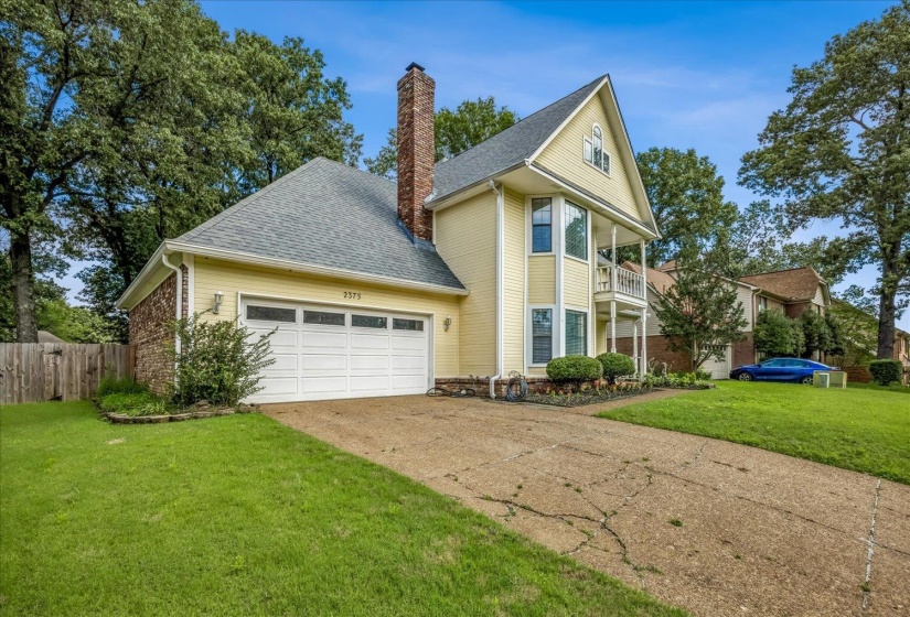 Two-story residence featuring light yellow siding, a two-car garage with paneling and transom windows, and a prominent brick chimney