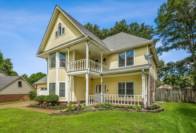 Two-story residence featuring light yellow siding, a two-level porch with white railings, and a prominent gable roofline