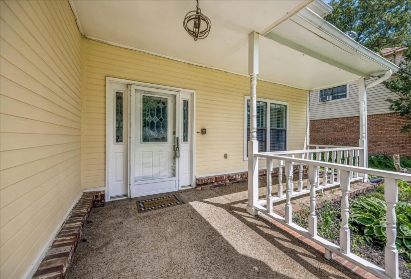 Covered front porch featuring yellow siding, white baluster railings, and a decorative glass entry door with sidelights
