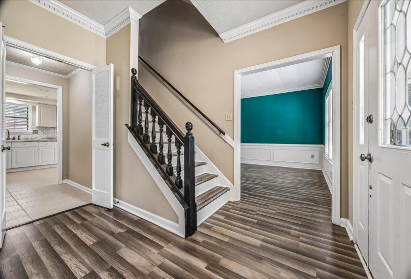 Entryway featuring wood-finish flooring, a dark wood staircase with white risers, and decorative crown molding
