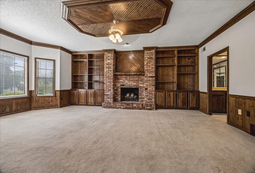 Spacious interior featuring a brick fireplace, extensive built-in wooden shelving, and warm wood paneling