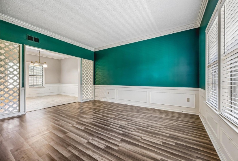 Spacious interior featuring wood-finish flooring, white paneled wainscoting, crown molding, and bright windows with blinds