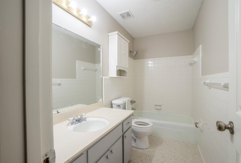 Bathroom featuring a built-in vanity with an integrated sink, a large wall-mounted mirror, overhead vanity lighting, a white tiled bathtub/shower combination, and white mosaic floor tiling