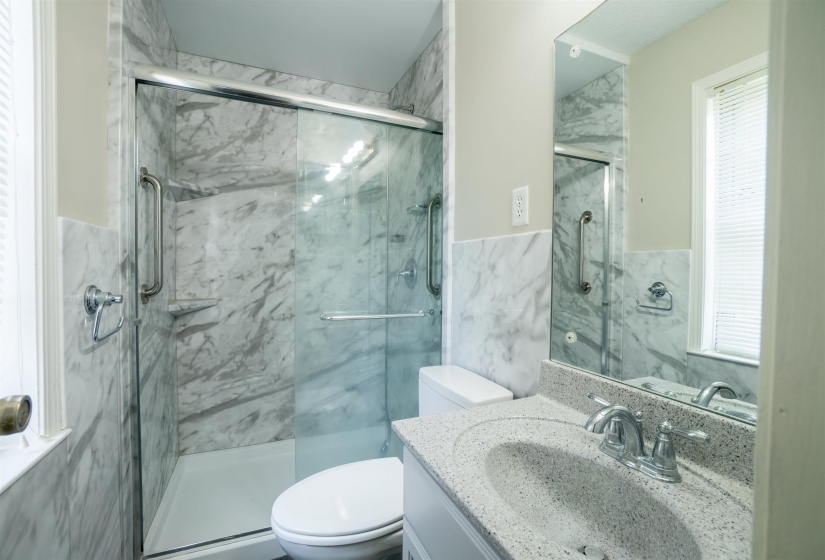 Bathroom featuring a walk-in shower with glass enclosure, marbled wall paneling, and a white base