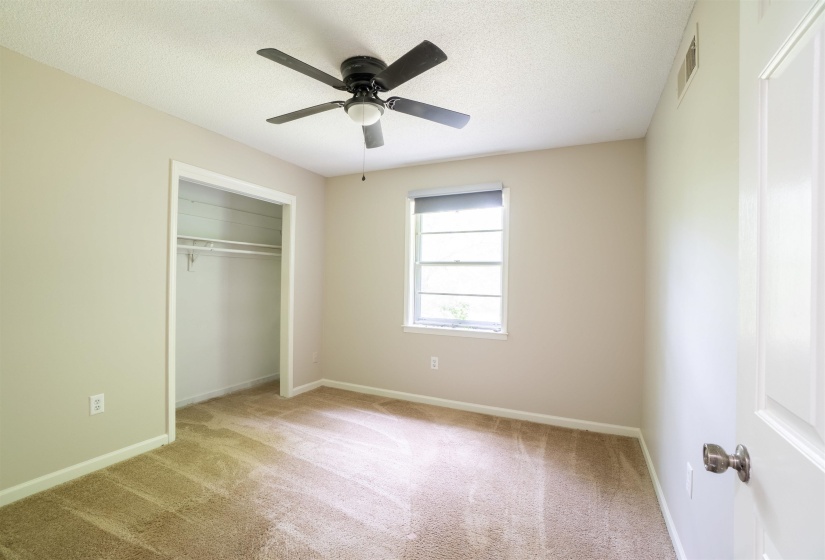 Carpeted room featuring a ceiling fan with integrated lighting, a window with a roller shade, and a closet with an integrated hanging rod and shelving