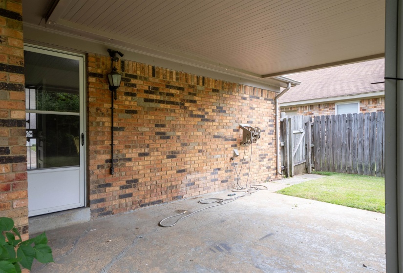 Covered concrete patio featuring a brick exterior wall, full-light entry door, and exterior lighting fixture