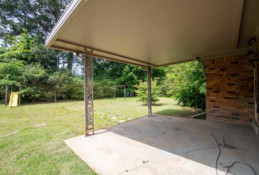Covered patio with concrete flooring, supported by decorative metal posts, opening to a spacious grassy yard