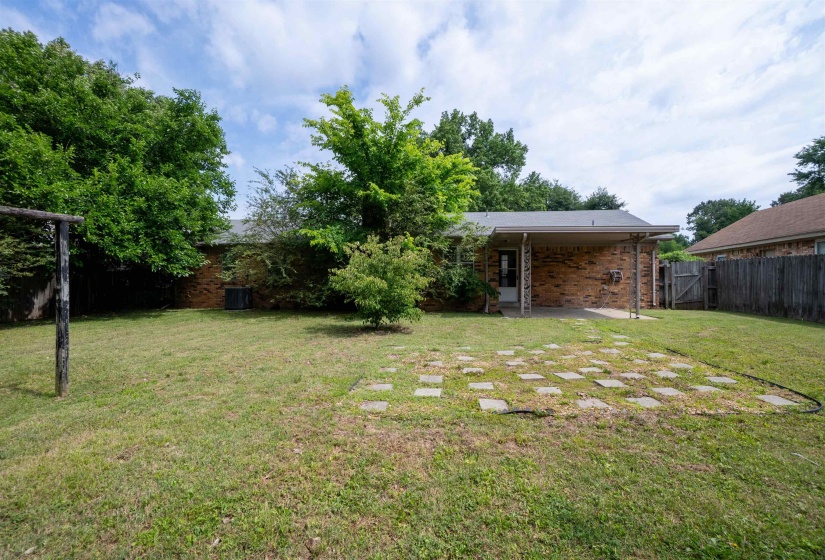Expansive backyard featuring a brick exterior, covered patio, privacy fencing, mature trees, and a stone paver patio area