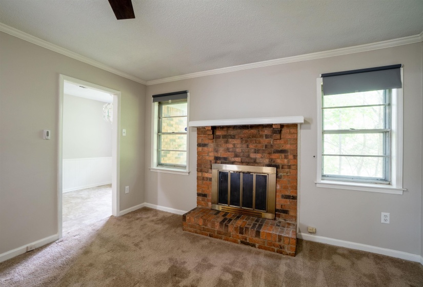 Living area featuring a brick fireplace with a brass firebox, a white mantle, and two windows with roller shades