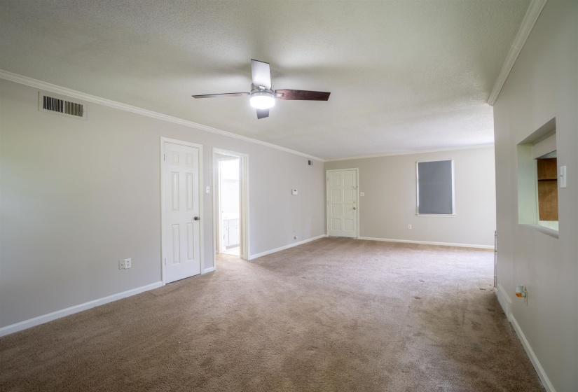 Spacious living area featuring neutral carpeting, light gray wall paint, white trim, and a ceiling fan with integrated lighting