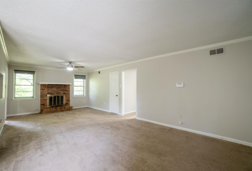 Spacious living area featuring a brick fireplace, twin windows, a ceiling fan, and light-toned wall paint