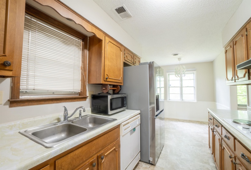 Kitchen featuring wood cabinetry, a double basin stainless steel sink, a stainless steel refrigerator, and light-colored countertops