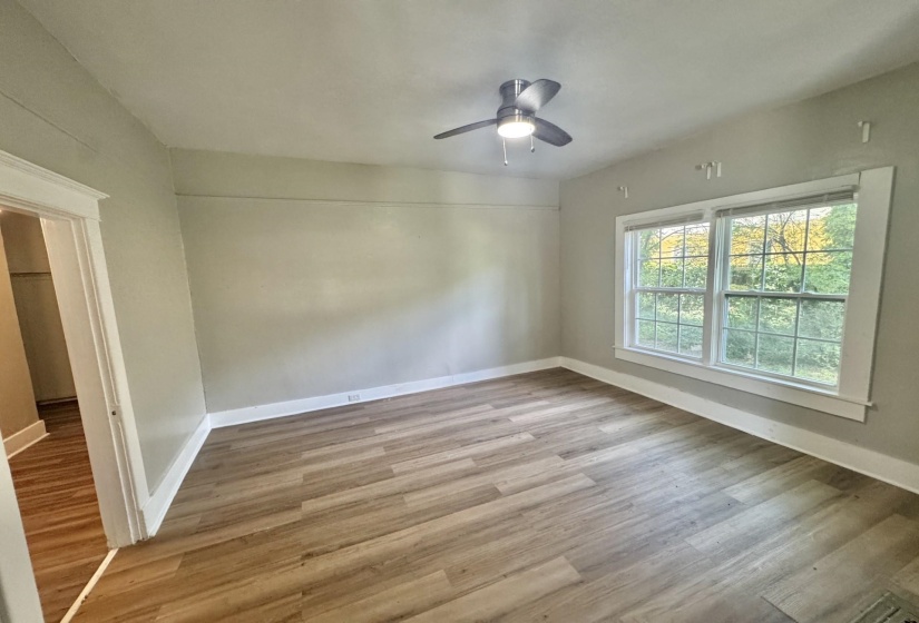 Spacious room featuring wood-finish flooring, light grey wall paint, and a modern ceiling fan with integrated lighting