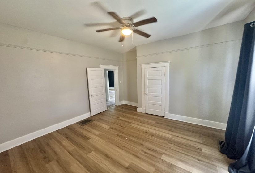 Expansive room with wood-finish flooring, a ceiling fan, and white trim