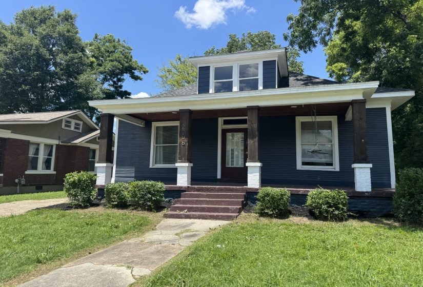 Residential exterior featuring a dark blue siding, white trim, and a prominent front porch with wood-finish columns on brick bases