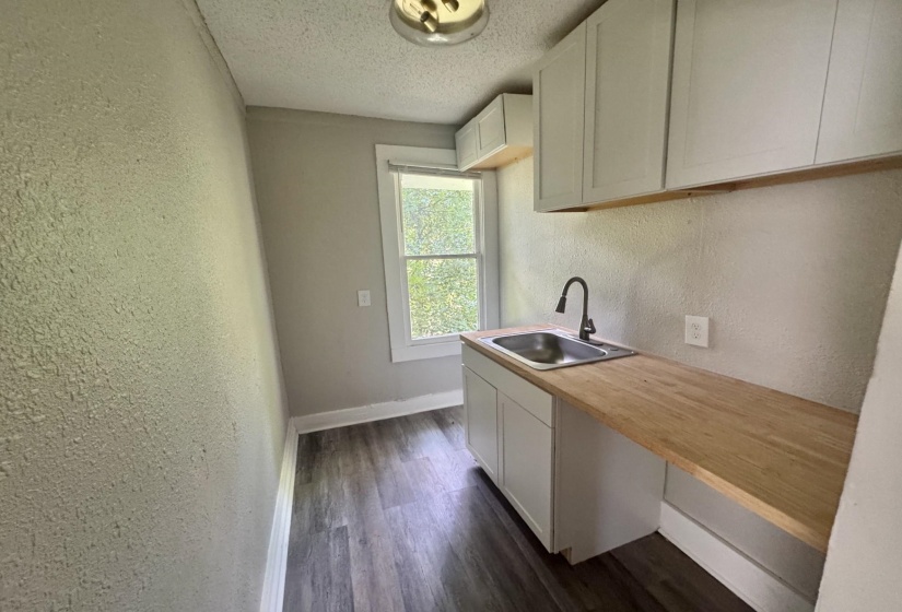 Utility area featuring wood-finish flooring, white cabinetry, a stainless steel sink with a dark-finish faucet, and a light wood-finish countertop