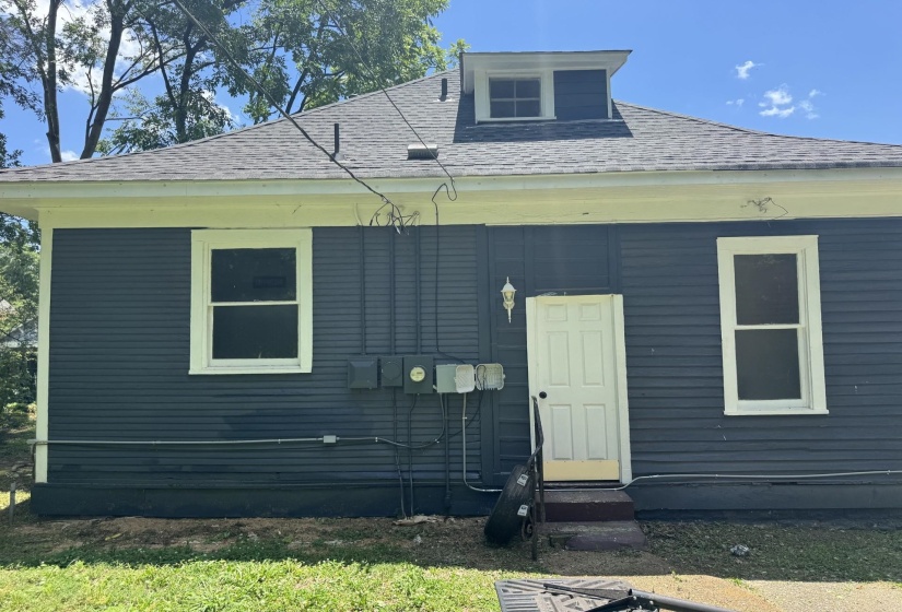 Dark-hued siding exterior featuring white trim, a dormer window, and a white paneled door