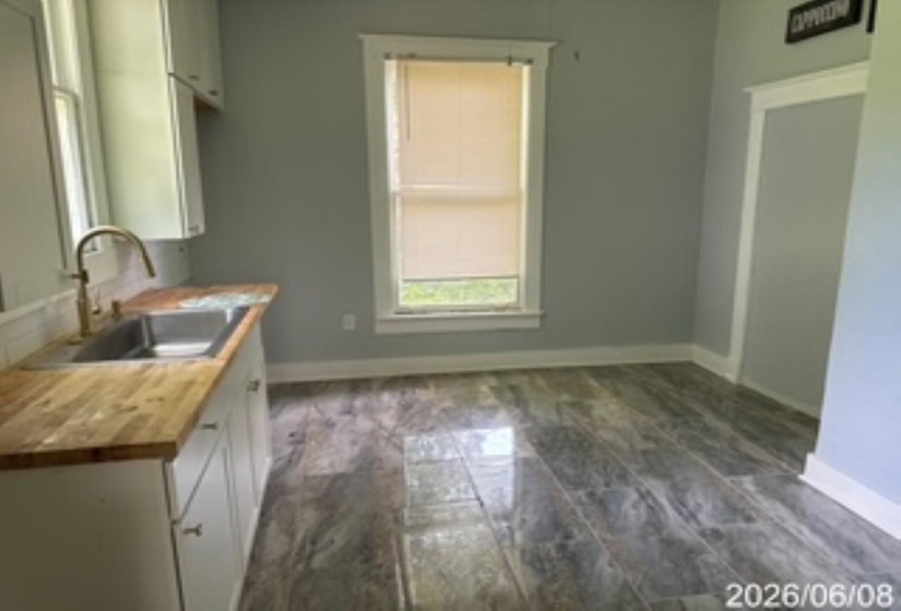 Kitchen area featuring wood-finish countertops, a stainless steel undermount sink with a brass-finish gooseneck faucet, white shaker-style cabinetry, and grey plank-style flooring