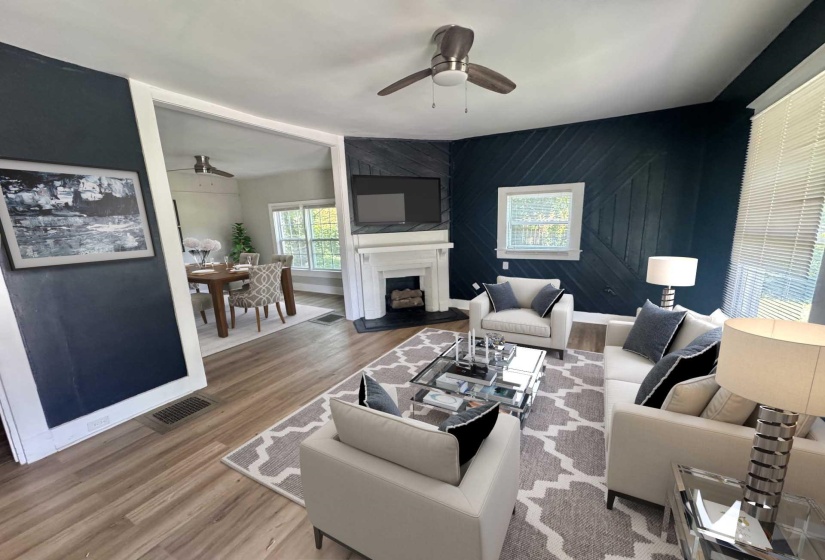 Living area featuring wood-finish flooring, a decorative fireplace with a white mantel, and a ceiling fan