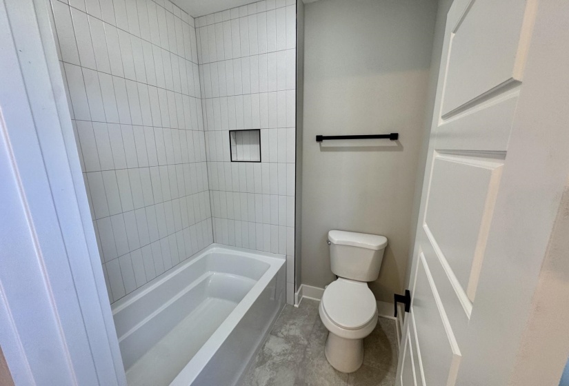 Full-sized tub and shower combination with vertical white tile surround and recessed niche