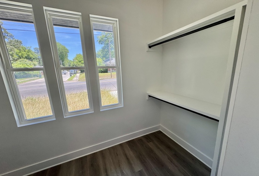 Room featuring three vertical windows with white trim, wood-finish flooring, and white baseboards