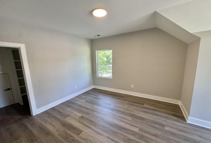 Spacious room featuring wood-finish flooring, neutral-toned walls, a single window, white trim, and a flush-mount ceiling light fixture