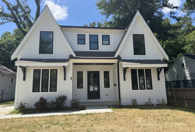 Contemporary farmhouse exterior featuring white siding, black-framed windows, a prominent gable roofline, black decorative brackets, and a black paneled front door