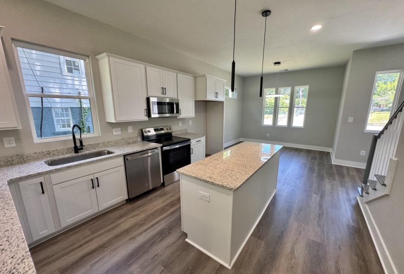Modern kitchen featuring white cabinetry, light-toned countertops, stainless steel appliances, a kitchen island, and wood-finish flooring