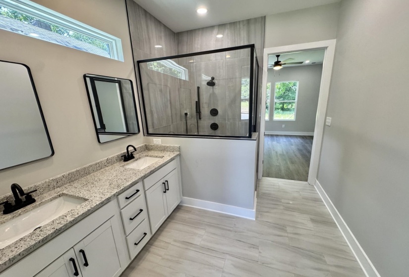 Bathroom featuring a double vanity with stone countertops and undermount sinks, matte black fixtures, framed mirrors, and a glass-enclosed shower with tile surround