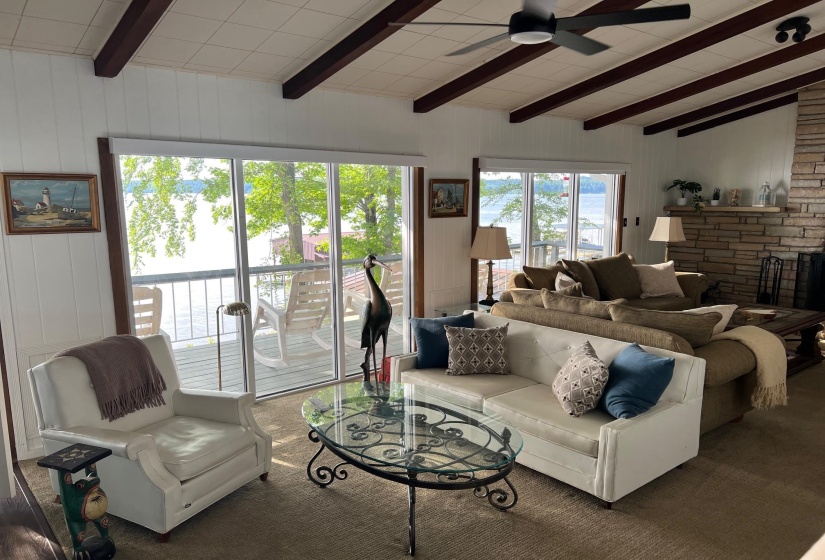 Spacious living area featuring large sliding glass doors, exposed ceiling beams, a stone-faced fireplace, and a ceiling fan